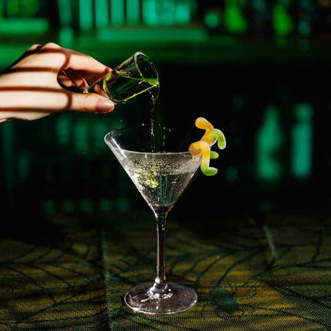 Someone pouring a shot of Corky's sour schnapps into a cocktail glass in a bar. 