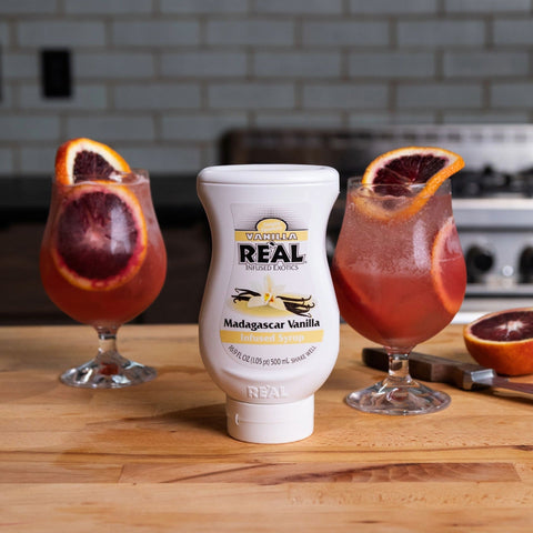 Two vanilla and grapefruit cocktails made using Reál Madagascar Vanilla Infused Syrup, with the Reál syrup bottle in between the two glasses. 
