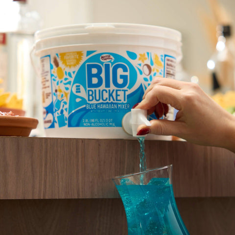 A person pouring a Blue Hawaiian cocktail from a Master of Mixes BIG BUCKET Blue Hawaiian mixer. 