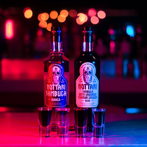4 shots of Nottari Sambuca with the two Nottari Sambuca bottles behind the shots. 