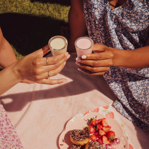 Two people holding alcoholic shots of Lustre vegan cream liqueur, in the flavours Pineapple Cream Rum and Strawberry Cream Tequila. 