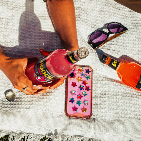 A person holding a bottle of Hooch Raspberry, an alcoholic pink lemonade, made with vodka and fruit juice. 