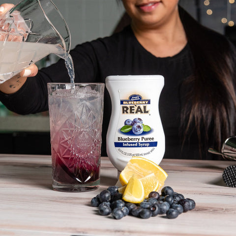 Someone making a cocktail using Real blueberry puree syrup, a gluten-free, vegan syrup. 