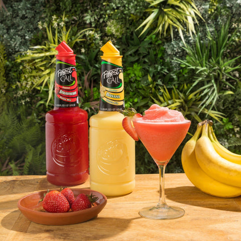 A bottle of Finest Call Strawberry Puree Mix with Finest Call Banana Puree Mix with a Frozen cocktail with fresh strawberries and bananas.