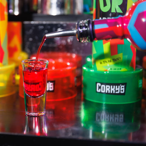 Someone pouring a shot of Corky's with different bottles of Corky's in the background.  