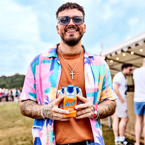 A man at a festival holding three cartons of Reef, a ready to drink, still, tropical alcopop. 