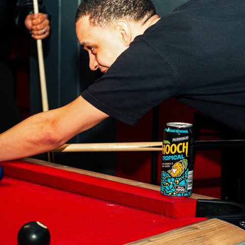 Person playing pool with a can of Hooch Tropical on the table, Hooch is a ready to drink, premixed vodka alcopop 