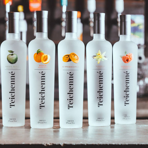 Five bottles of Teichenne schnapps in flavours: green apple, peach, butterscotch, vanilla  raspberry all lined up on a bar. 