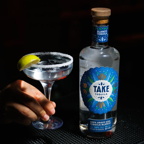 Bottle of Take Tequila Blanco with a cocktail and lemon wedge on a bar.