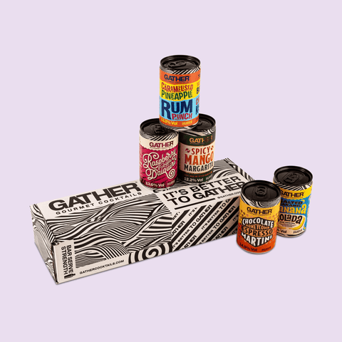 A collection of canned cocktails from the GATHER brand displayed in front of a box labelled GATHER mixed pack. The cans are adorned with various colourful labels indicating different flavours.