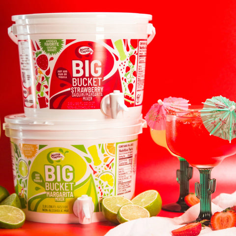 Master of mixes strawberry and margarita big buckets next to two cocktails with mini umbrellas. 