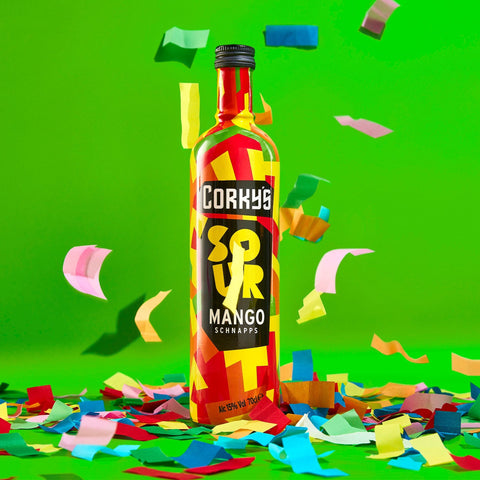 A bottle of Corky's sour mango schnapps on a green background with multi-coloured confetti. 