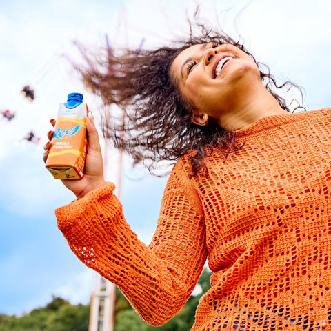 A person at a festival holding a carton of Reef, a ready to drink, still, tropical alcopop. 