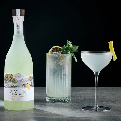 Two yuzu cocktails made with Asuki Yuzu Citrus Liqueur, with the bottle of Asuki placed next to the two cocktails. 