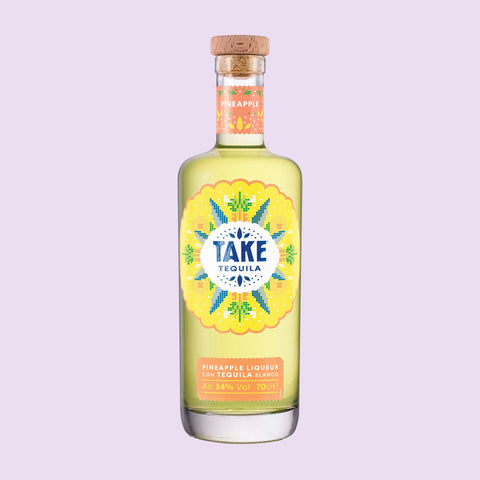 A bottle of Take Tequila Pineapple Liqueur with a vibrant yellow label with a light purple background. 