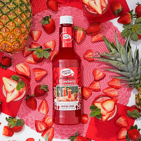 A bottle of Master Of Mixes Strawberry cocktail mixer, surrounded by ripe strawberries, a pineapple, and a glass filled with the strawberry mixer and ice.
