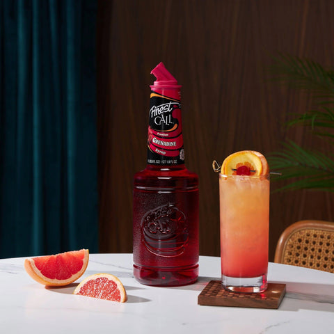 A Tequila Sunrise cocktail made with Finest Call Premium Grenadine Syrup, with the Finest Call bottle placed next to the cocktail. 