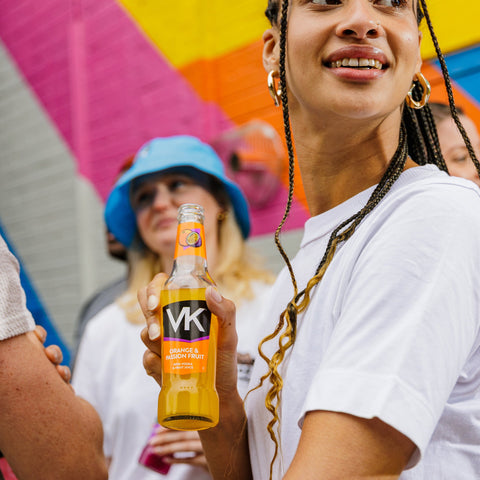 Someone holding a bottle of VK orange and passionfruit, a vodka alcopop in a group/festival setting. 