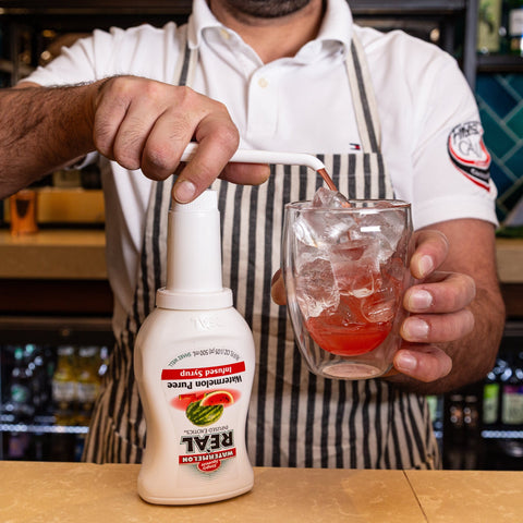 Someone squeezing Reál watermelon syrup into a glass, Reál syrups are perfect for cooking & baking, making cocktails or mocktails and dirty sodas. 
