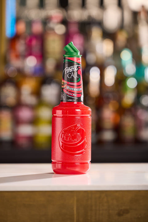 Red bottle of Finest Call Watermelon Puree with green cap on a bar counter, blurred bottles in the background