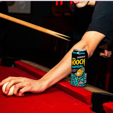 Someone playing pool drinking a can of Hooch Tropical, a premixed ready to drink alcopop. 