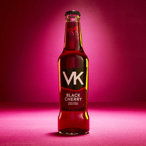 A glass bottle of VK Black Cherry flavored alcopop with a pink background.