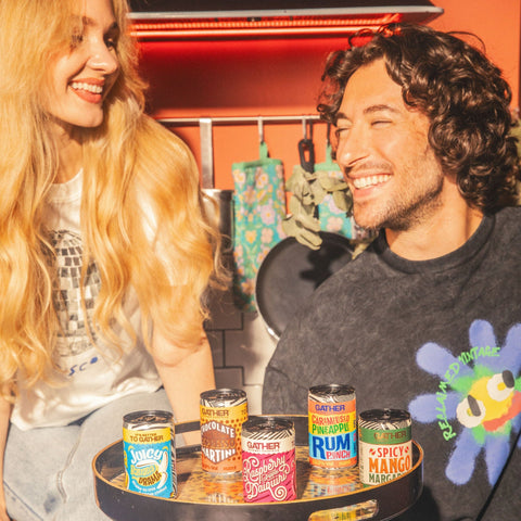 Two people smiling holding a tray of GATHER cocktails in a kitchen background. 