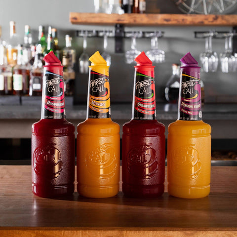 Four bottles of Finest Call Fruit Purees on a bar counter with a blurred bar background.