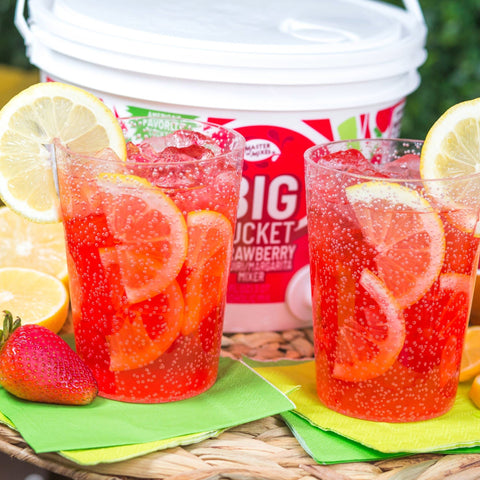 Two pink drinks with lemons and Master of Mixes Strawberry big bucket in the background. 