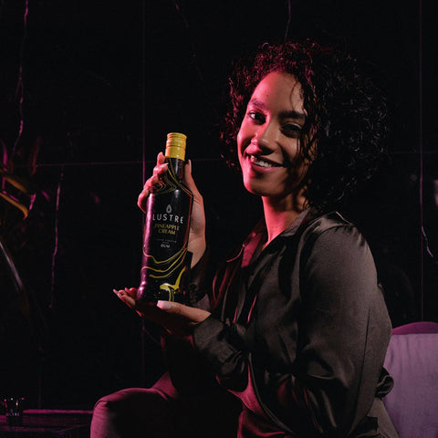 A woman holding a bottle of Lustre Pineapple Cream Rum, a vegan cream liqueur. 
