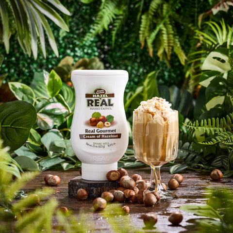 A hazelnut coffee that's been made using Re'al Cream of Hazelnut Syrup with the Re'al bottle placed next to the drink. 
