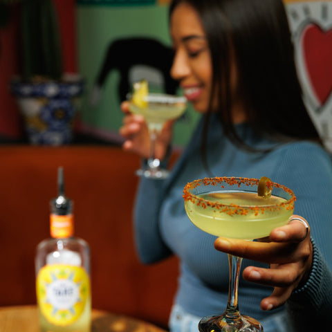 Woman holding a cocktail in a bar setting with a bottle of Take Tequila on the table.