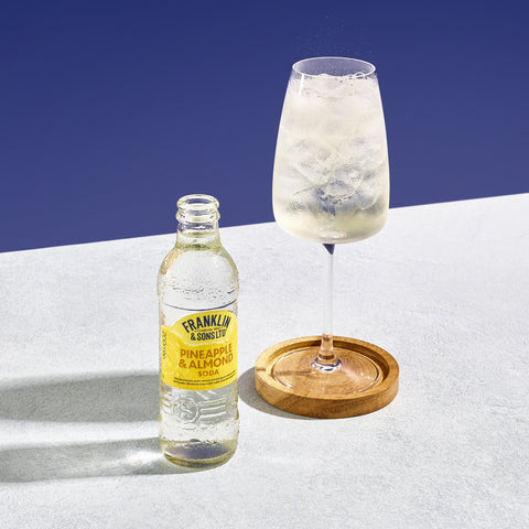 A bottle of Franklin & Sons premium pineapple and almond soda next to a drink where Franklin & Sons has been used as a mixer. 