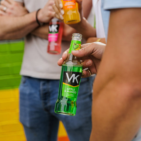 A group of people stood talking all holding a bottle of VK, a ready to drink vodka alcopop. 