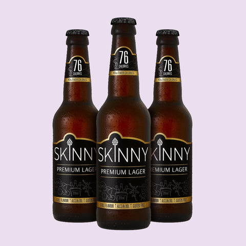 Three bottles of Skinny Premium Lager on a light purple background