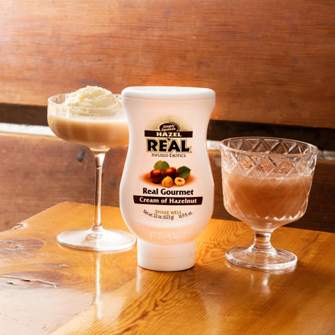 Two hazelnut drinks made using Re'al Cream of Hazelnut Syrup, with the Re'al syrup bottle placed in between the drinks. 