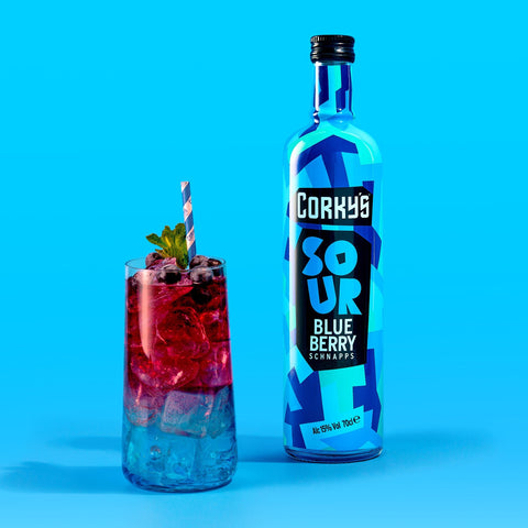 A bottle of Corky's sour blueberry schnapps next to a cocktail made with the blueberry schnapps on a bright blue background, Corky's is also perfect for easy shots. 