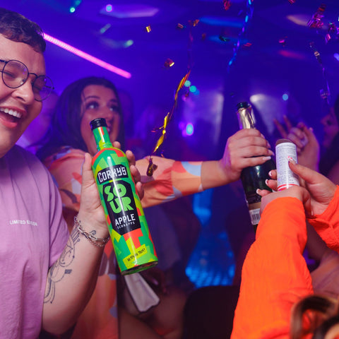 Someone holding a bottle of Cork's sour apple schnapps at a party. 