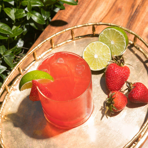 Red cocktail with lime and strawberries on a gold tray outdoors