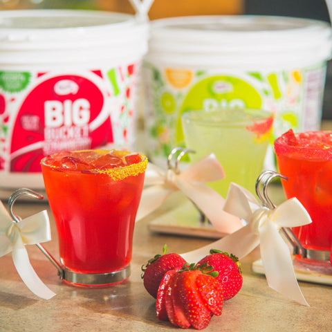 Three drinks with ribbon and strawberries with Master of Mixes big buckets in the background. 
