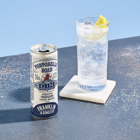 A ready to drink can of Franklin & Sons Premium Indian Tonic & Portobello Road Gin placed next to a filled glass of tonic water with ice and a slice of lemon on a coaster.
