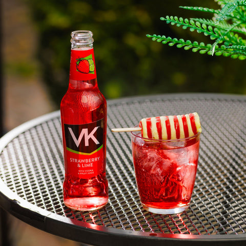 A bottle of VK strawberry and lime, a ready to drink alcopop, next to a glass of strawberry and lime with a twister ice lolly on top of the glass. 