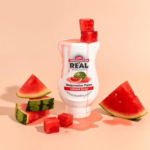 A bottle of Reál Watermelon Puree Infused Syrup, with watermelons around the bottle. 