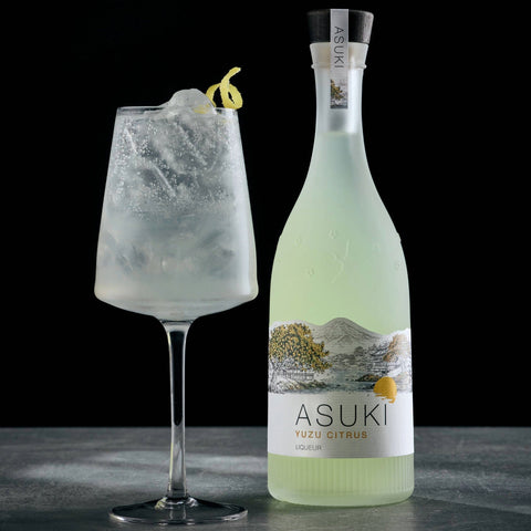 A yuzu spritz cocktail made with Asuki Yuzu Citrus Liqueur, with the Asuki bottle placed next to the cocktail. 
