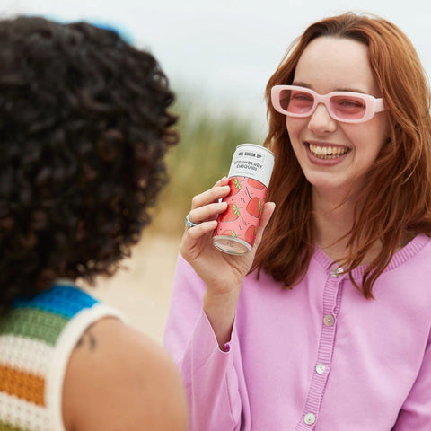 A woman talking and laughing drinking and All Shook Up Strawberry Daiquiri can. 