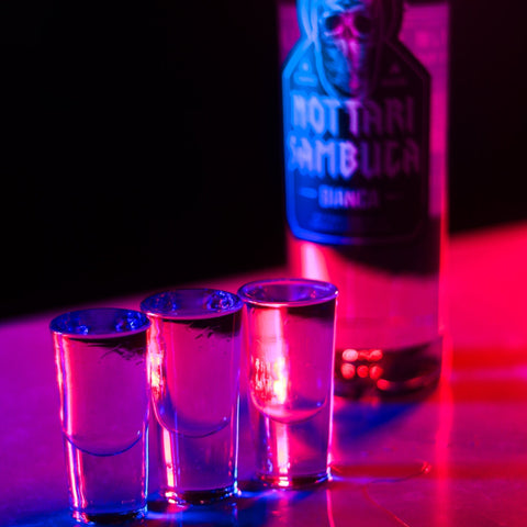 Three alcoholic shots of Nottari Bianca Sambuca with the Nottari bottle behind the shots. 