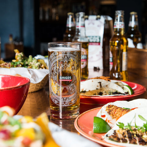Amigos Tequila Flavoured Beer in an Amigos branded pint glass surrounded by Mexican food