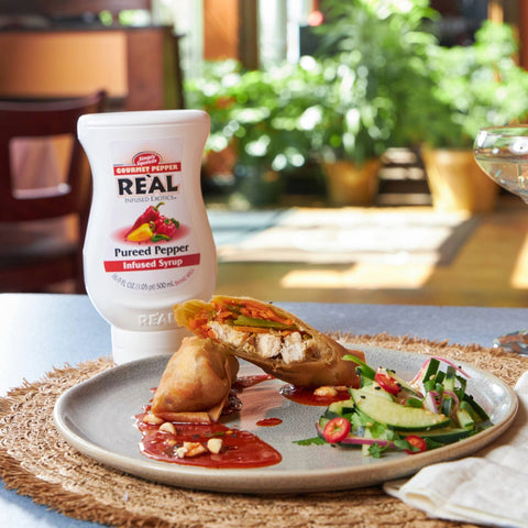 A plate of food with a chilli sauce that has been made using Re'al Gourmet Pepper Puree Infused Syrup, with the Re'al bottle next to the plate of food. 