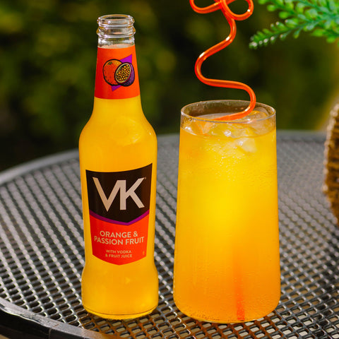 A bottle of VK orange and passionfruit next to a glass of orange and passionfruit VK with an orange straw. 
