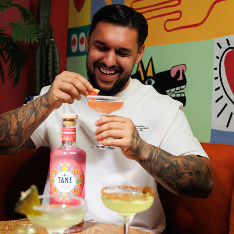 Man enjoying a drink in a colourful room with a colourful wall with a bottle of Take tequila on the table. 